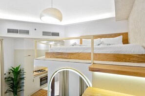A compact, modern bedroom with bunk beds, a small kitchenette, and a mirror with integrated lighting.