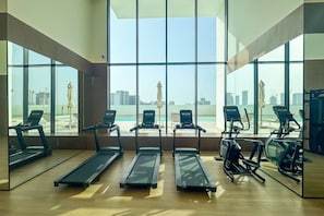 A gym with treadmills, elliptical machines, and exercise bikes, large windows with a city view.