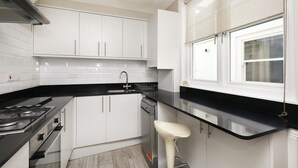 A modern kitchen with white cabinets, a black countertop, a gas stove, and a dishwasher. - Charming 1BR Flat in Quiet S Kensington (London)
