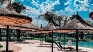 Ein Strandresort mit Reetdachschirmen, Liegestühlen und einem Pool.