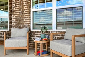 Un espace patio comprenant deux chaises grises à revêtement rembourré, une petite table ronde avec un pot de plante et un mur en briques.