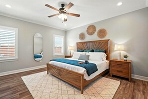 Une chambre avec un lit en bois, un ventilateur de plafond, deux tables de chevet avec des lampes et un grand miroir au mur.