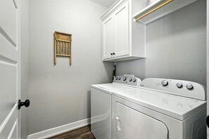 Une buanderie équipée d’un lave-linge et d’un sèche-linge à chargement frontal, d’un panier en bois fixé au mur et d’un meuble blanc placé au-dessus du sèche-linge.