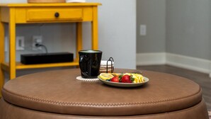 A brown leather ottoman with a plate of fruit and a black mug on a coaster.