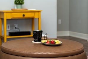 A brown leather ottoman with a plate of fruit and a black mug on a coaster.