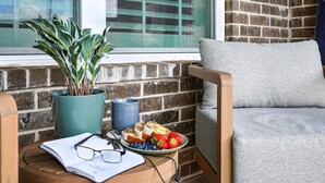 A cozy seating area with a cushioned chair, a small table with a book, glasses, and a plate of food.