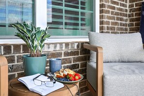 A cozy seating area with a cushioned chair, a small table with a book, glasses, and a plate of food.
