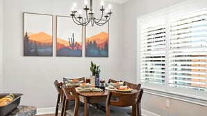 A dining area with a table set for four, surrounded by chairs, a chandelier, and artwork on the wall.
