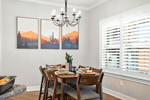 A dining area with a table set for four, surrounded by chairs, a chandelier, and artwork on the wall.