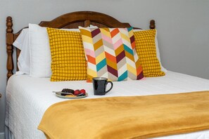 Una cama con cabecera de madera, ropa de cama blanca y una manta amarilla.