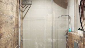 A modern bathroom with a glass-enclosed shower, a white toilet, and a sink with a mirror above it.