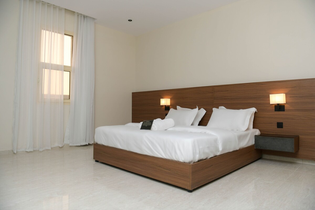 A modern hotel room with a wooden bed frame, white bedding, and two wall-mounted reading lamps.