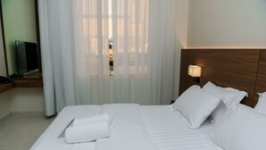 A hotel room with a large bed, white linens, a flat-screen TV, and a window with sheer curtains. - Arjan Park Al Qadisiyah (Riyadh)