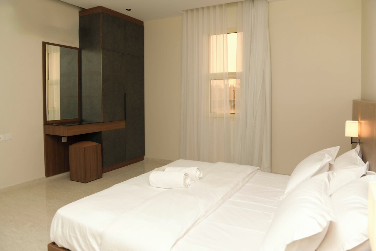 A hotel room with a bed, a large mirror, a desk, and a window with curtains.