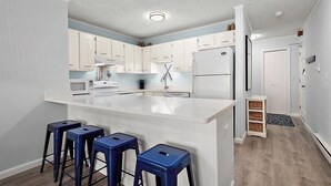 A modern kitchen with white cabinetry, a central island with stools, a refrigerator, and a microwave.