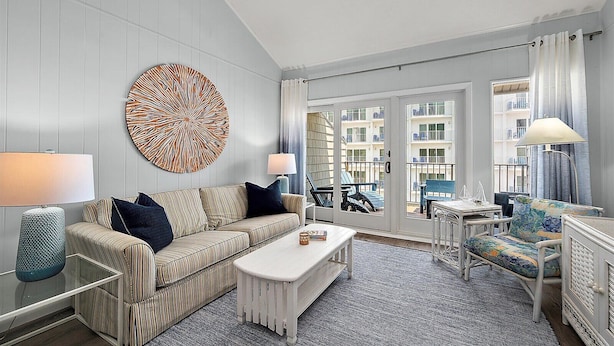 A modern living room with a striped sofa, a round wall art piece, a white coffee table, and a view of balconies through a glass door.