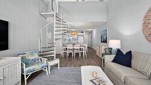 A modern interior with a spiral staircase, a dining area, and a living space with a sofa and a TV.