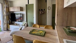A modern living space with a dining area, a television mounted on the wall, and a kitchen area visible through a sliding door. - Stunning renovated T2, air conditioning, parking, balcony - City and mountain views (Aix-les-Bains)