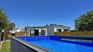 Una casa moderna amb piscina, zona de barbacoa i tanca de fusta.