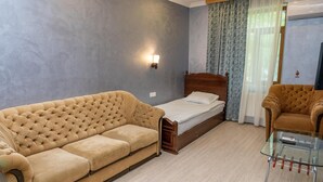 A room with a large beige sofa, a wooden bed, a glass table, and a small armchair. - Qabala Semerena Riverside Hotel (Gabala)