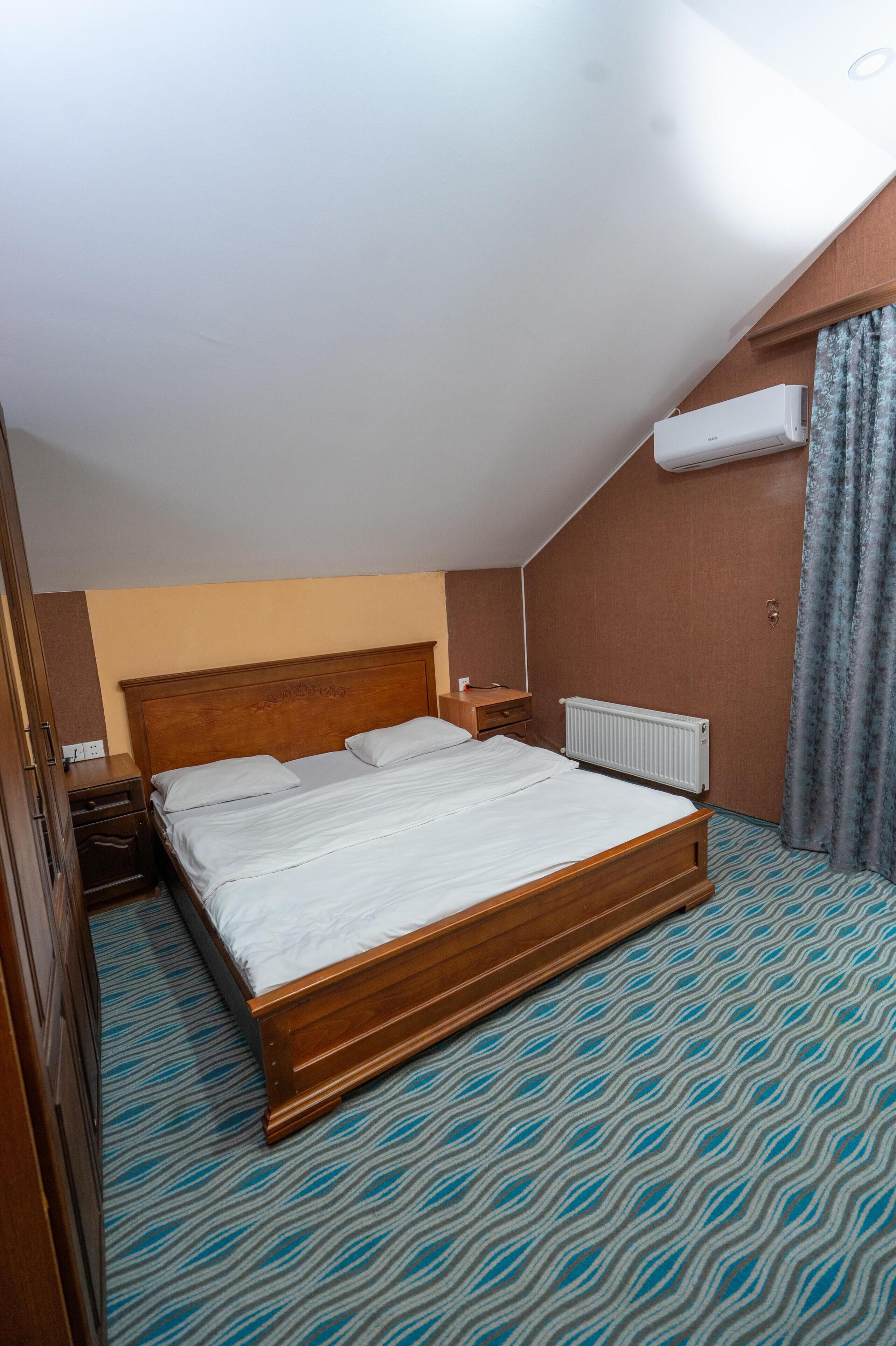 A bedroom with a wooden bed, a nightstand, a dresser, an air conditioning unit, and a patterned carpet.