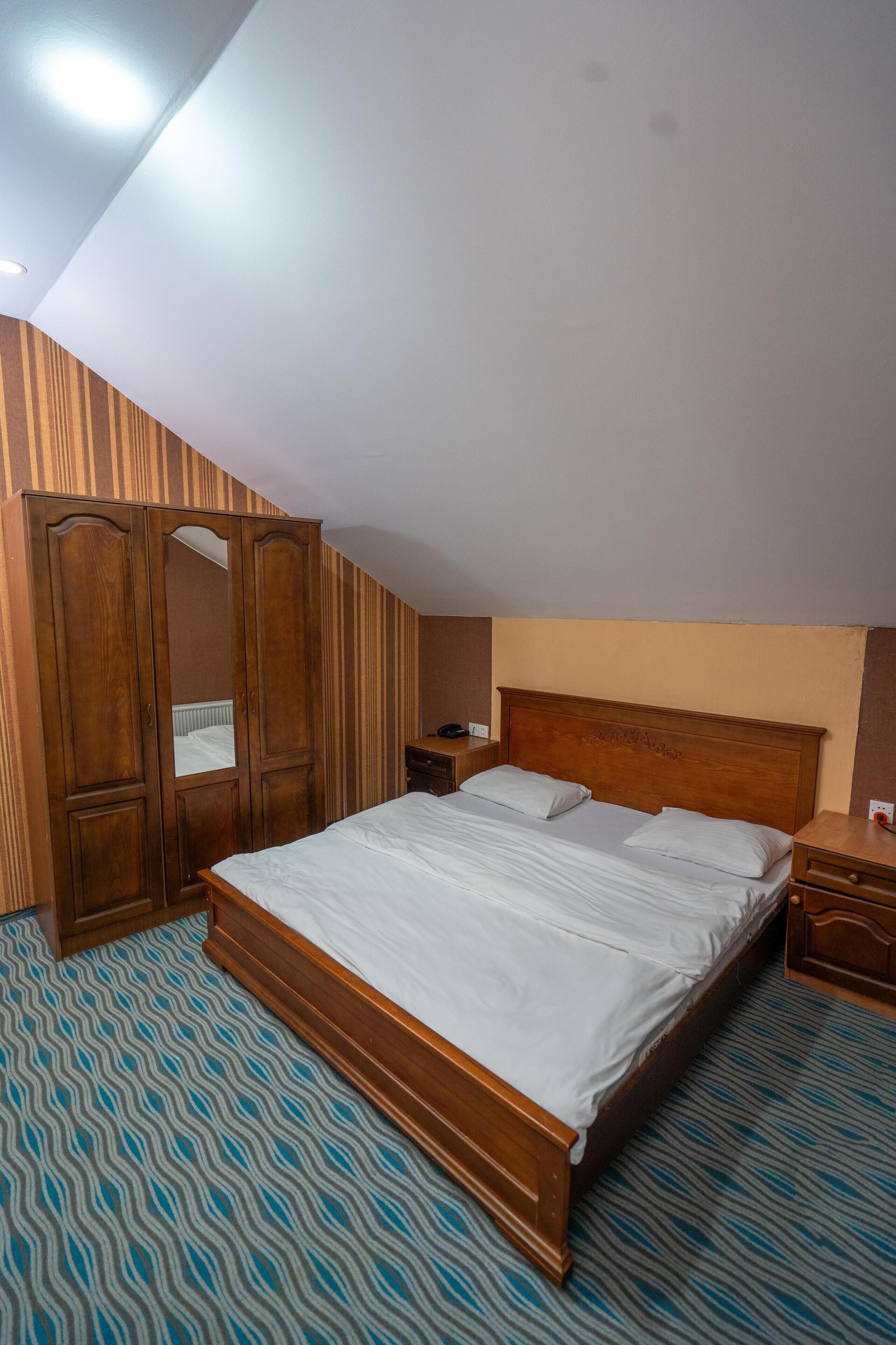 A bedroom with a wooden bed, a wardrobe, a nightstand, and a patterned carpet.