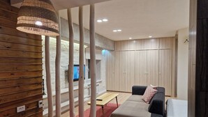 A modern living room with a sofa, a small table, and a TV. There is a wooden wall and a wardrobe in the background. - Cozy apartment in the city center with AC & Wi-Fi (Tashkent)