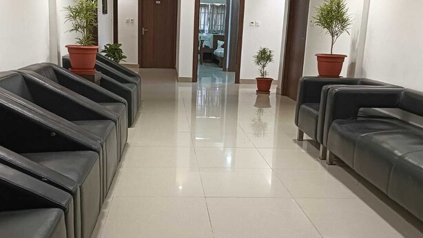 A clean, modern waiting area with black leather seating and potted plants. - Hotel Vrindavan Palace (Giridih)