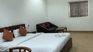 A hotel room with a bed, a chair, a small table, and a window with curtains. - Hotel Vrindavan Palace (Giridih)