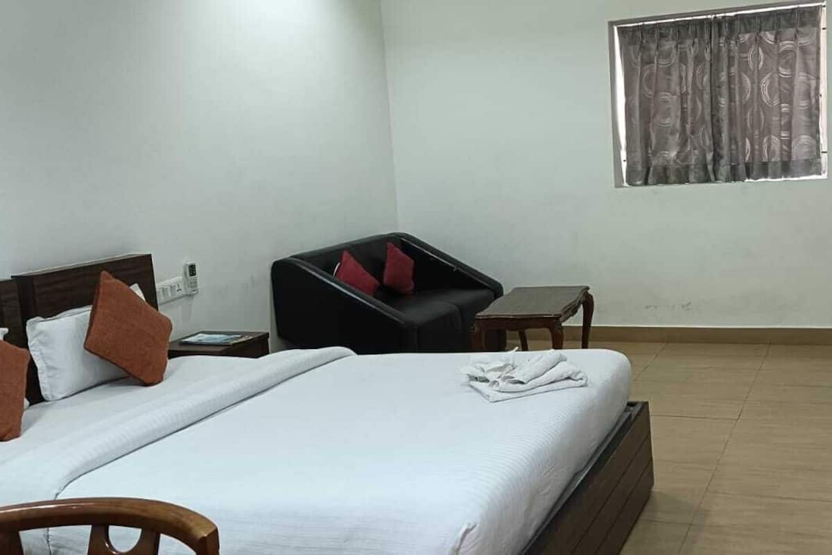 A hotel room with a bed, a chair, a small table, and a window with curtains.