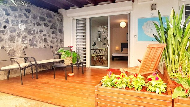 A covered patio with a stone wall, wooden flooring, and outdoor furniture. - Quiet studio for two, wheelchair accessible, near golf and beaches (Les Avirons)