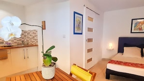 A compact hotel room with a wooden dining table, a single bed, a nightstand with a lamp, and a bathroom visible in the background. - Quiet studio for two, wheelchair accessible, near golf and beaches (Les Avirons)