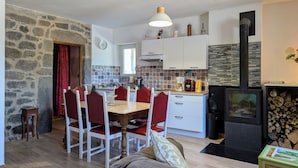 A cozy kitchen with a stone wall, a dining area with red chairs, a stove, and a clock on the wall. - Rustic stay near Estables and Puy-en-Velay (Saint-Front)