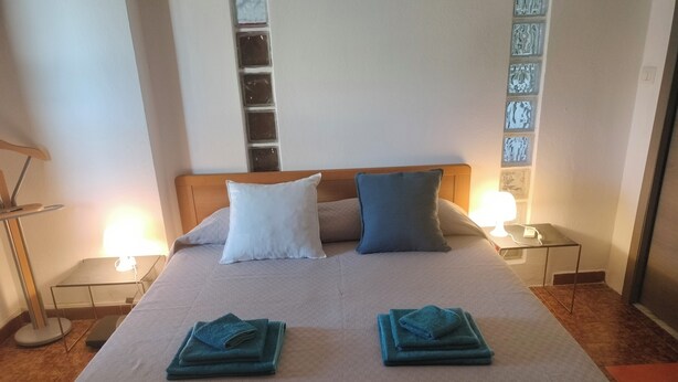 A neatly made bed with two pillows, a bedside table with a lamp, and a wall with decorative tiles.