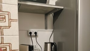 Ett litet, praktiskt kök med en mikrovågsugn, vattenkokare och kaffebryggare på en hylla, ett kylskåp och en vägg med ett mönstrat tapet.