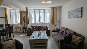 A living room with a sofa, a coffee table, a dining table with chairs, and a lamp.