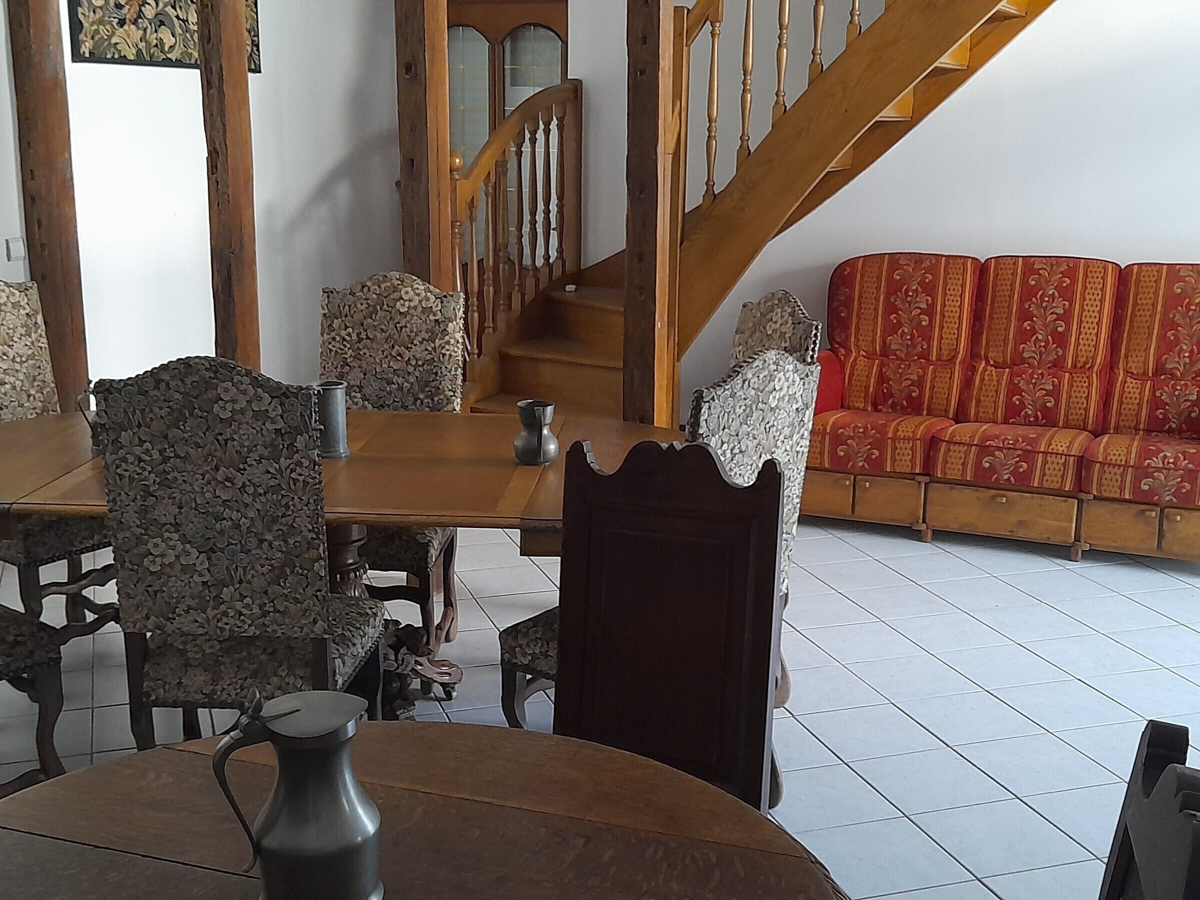 Un coin repas avec une table et des chaises en bois, un canapé agrémenté de coussins à motifs et un escalier avec des rampes en bois.