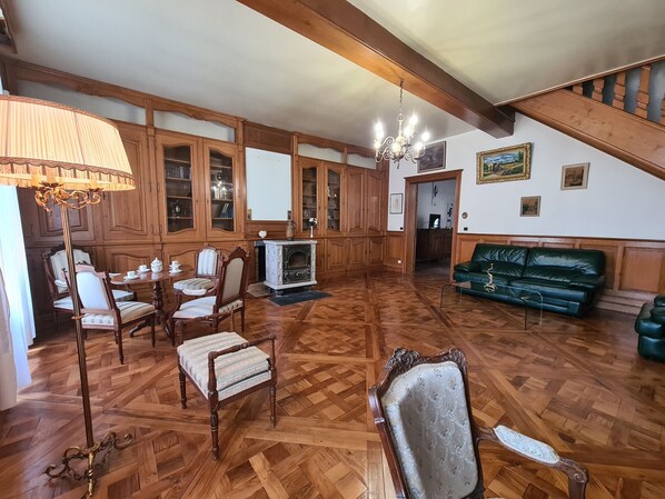 A spacious living room with wooden paneling, a green sofa, a dining area with a table and chairs, and a staircase leading upstairs. - Spacious Family Home with Pool and Parking in Saint-Gaultier (Saint-Gaultier)