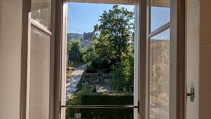 Une vue à travers la fenêtre d’un bâtiment en pierre, avec un sentier qui mène à une colline.