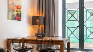 Un comedor con una mesa de madera, sillas de malla metálica, una lámpara negra y un cuadro en la pared.