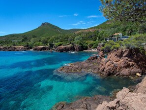A coastal landscape with clear turquoise waters, rocky shores, and a hill in the background.
