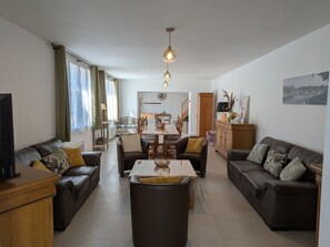 A modern living room with leather sofas, a dining table, and a kitchen in the background. - Charming Family Cottage near Orléans with Garden (Boulay-les-Barres)