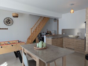 Une cuisine moderne avec des meubles en bois, une cuisinière encastrée et un coin repas agrémenté d’un baby-foot.