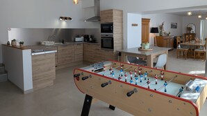 A modern kitchen with a foosball table, wooden cabinets, and a dining area with a table and chairs.