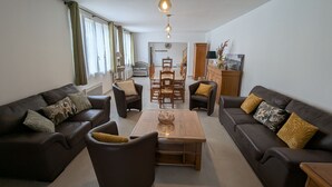 A modern living room with dark leather sofas, a wooden coffee table, and a dining area with wooden chairs and a table.