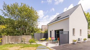 Une maison moderne avec une allée pavée, un petit patio doté de meubles d’extérieur et une pelouse bien entretenue.