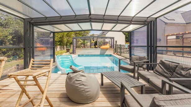 Un espace extérieur abrité par des parois de verre, comprenant une piscine, une terrasse en bois et des sièges.