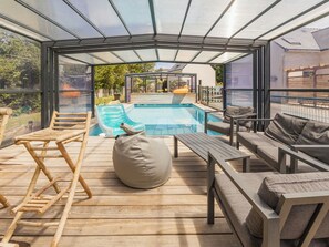 Un espace extérieur abrité par des parois de verre, comprenant une piscine, une terrasse en bois et des sièges.