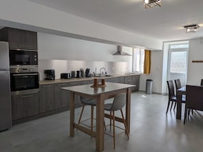 Et moderne køkken med en central ø, integrerede hårde hvidevarer og et spiseområde med stole.