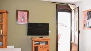 Ein Wohnzimmer mit Flachbildfernseher auf Holzfuß, einer Tür, die nach draußen führt, und einem gerahmten Bild an der Wand.